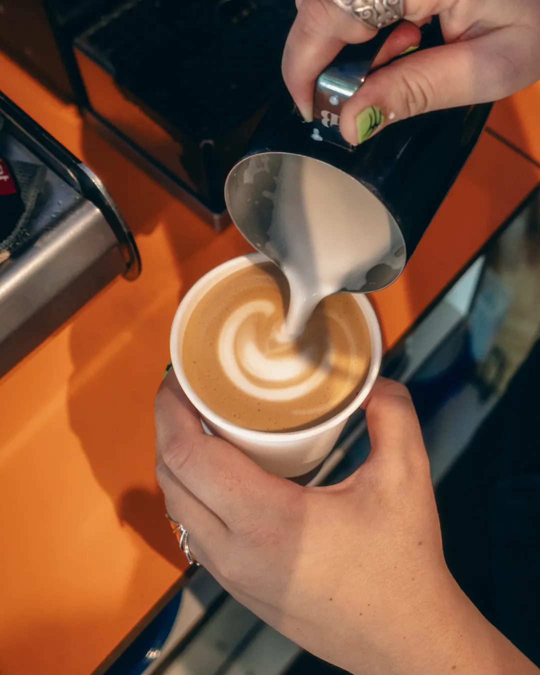 Barista pouring milk into a takeaway cup at the orange bar